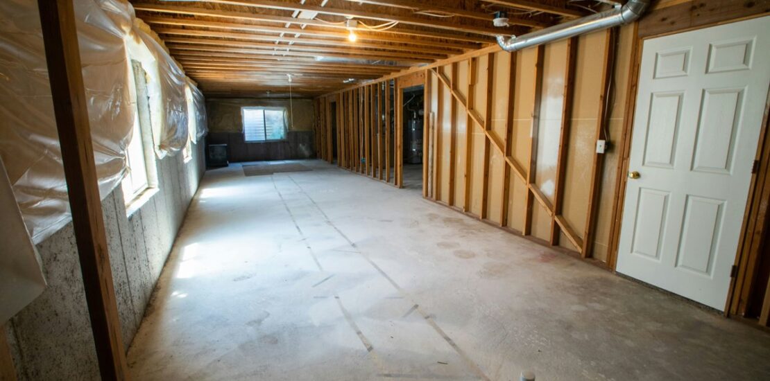 Unfinished basement interior with exposed framing and vapor barrier